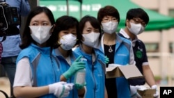 South Korean health workers from a community health center wearing masks as a precaution against MERS, Middle East Respiratory Syndrome, virus, wait to check examinees' temperature and to sanitzie their hands at a test site for a civil service examination