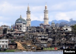 FILE - A sign that reads "I love Marawi" is seen in front of damaged houses, buildings and a mosque inside a war-torn Marawi city, southern Philippines, Oct. 26, 2017.