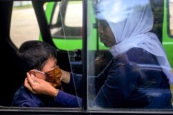 Seorang ibu memasang masker wajah untuk anaknya di dalam angkutan umum di Bogor, Jawa Barat, Rabu, 8 April 2020. (Foto: AFP)