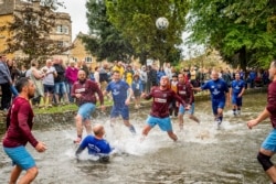 Para pesepakbola berebut bola di Sungai Windrush dalam pertandingan sepak bola sungai tradisional tahunan di desa Cotswolds, Bourton-in-the-Water, Inggris, Senin, 30 Agustus 2021. (Ben Birchall/PA via AP)