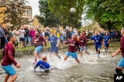 Para pesepakbola berebut bola di Sungai Windrush dalam pertandingan sepak bola sungai tradisional tahunan di desa Cotswolds, Bourton-in-the-Water, Inggris, Senin, 30 Agustus 2021. (Ben Birchall/PA via AP)