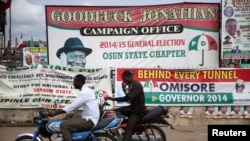 FILE - Men ride past motorcycles in front of a Peoples Democratic Party office at the Osun state governorship election in Osogbo, southwest Nigeria, Aug. 9, 2014.