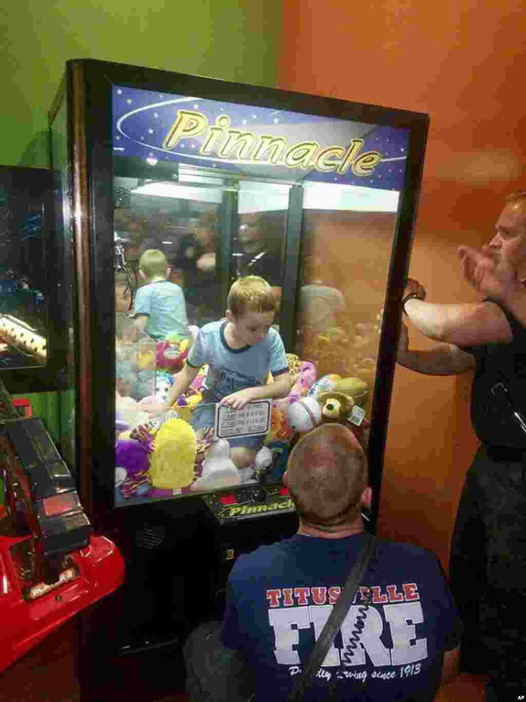 This photo made available by the Titusville Fire and Emergency services shows fire fighters attempting to rescue a boy who crawled inside a claw-style vending machine, in Titusville, Florida,&nbsp; Feb. 7, 2018.