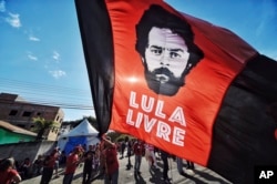 FILE - A supporter of former Brazilian President Luiz Inacio Lula da Silva waves a banner decorated with an image depicting da Silva and message that reads in Portuguese: "Free Lula," in front of the Federal Police Department where he is serving jail time