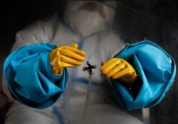 Seorang petugas kesehatan yang mengenakan alat pelindung diri membersihkan sarung tangannya sebelum melakukan tes reaksi berantai polimerase (PCR). (Foto: Reuters)