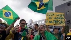 A demonstrator holds up a sign that reads in Portuguese "Lula, a thief's place is in prison" as people shout slogans against Brazil's former President Luiz Inacio Lula da Silva in front of the Federal Police Department in Curitiba, Brazil, April 6, 2018.