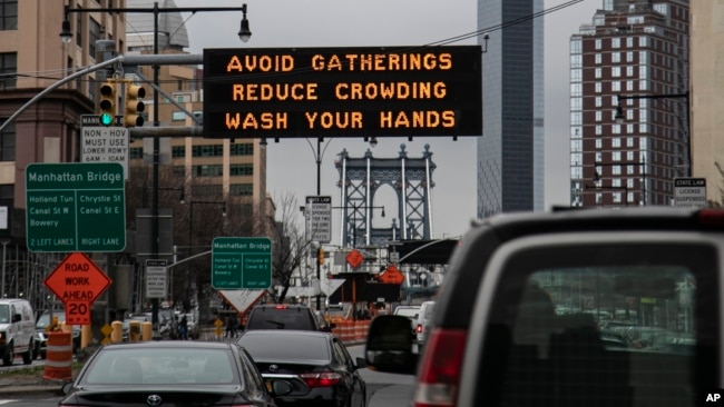 In this March 19, 2020, file photo, the Manhattan bridge is seen in the background of a flashing sign urging commuters to avoid gatherings, reduce crowding and to wash hands in the Brooklyn borough of New York. The coronavirus pandemic is leading to infor