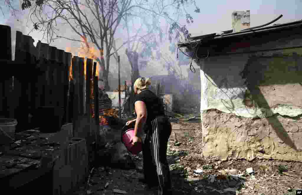 زنی در تلاش برای فرونشاندن آتشی که در پی انفجار به خانه&zwnj;اش افتاده. روزهای شنبه و یکشنبه، به رغم اعلام آتش&zwnj;بس، چند انفجار در شرق اوکراین روی داد &ndash; دونتسک، ۱۶ شهریور ۱۳۹۳