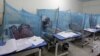 Một người phụ nữ giữ con trai, mắc bệnh sốt xuất huyết, khi ngồi dưới màn chống muỗi trong một bệnh viện địa phương ở Rawalpindi, Pakistan.
