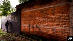 Archivo - En esta foto del 10 de octubre de 2019, un policía hace guardia al lado de un graffiti con el nombre de una pandilla como parte de la patrulla rutinaria en Lourdes, La Libertad, El Salvador.
