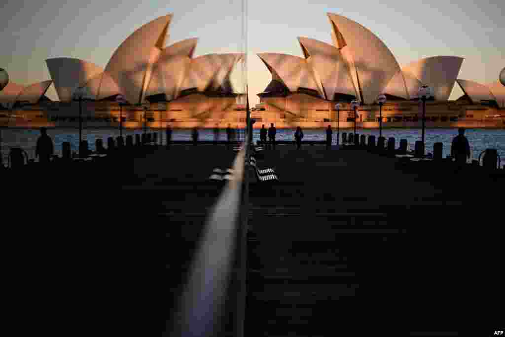 Sunset hues fall on the landmark Sydney Opera House as it is seen in a reflection from Circular Quay, usually packed with tourists, in Sydney, Australia.