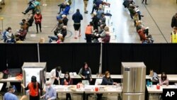 FILE - People work near refrigerators used to store the Pfizer vaccine for COVID-19, as patients who have received the shot sit in an observation area at a clinic in an Amazon.com facility in Seattle, Jan. 24, 2021.