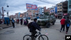 Un hombre con una máscara facial protectora contra la propagación del nuevo coronavirus, pasa su bicicleta frente a un vehículo blindado militar que patrulla las calles durante una cuarentena en El Alto, Bolivia, el viernes 20 de marzo de 2020. 