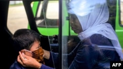 Seorang ibu memasang masker wajah untuk anaknya di dalam angkutan umum di Bogor, Jawa Barat, Rabu, 8 April 2020. (Foto: AFP)