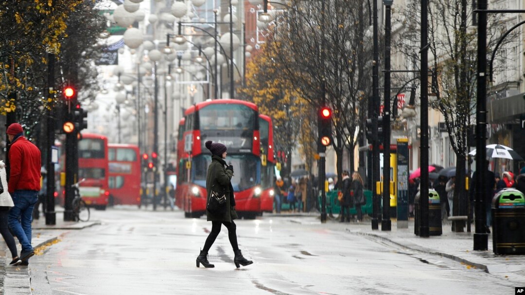 Seorang perempuan berjalan menyeberangi Jalan Oxford di London yang dipenuhi para pengunjung, di tengah hujan salju, Minggu, 10 Desember 2017. (AP Photo/Alastair Grant)