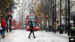 Seorang perempuan berjalan menyeberangi Jalan Oxford di London yang dipenuhi para pengunjung, di tengah hujan salju, Minggu, 10 Desember 2017. (AP Photo/Alastair Grant)