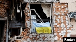 (FILE) A Ukrainian national flag hangs from a balcony of a destroyed civilian building in Irpin, Ukraine June 16, 2022.