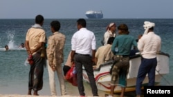 FILE - People stand on the beach as the Galaxy Leader commercial ship, seized by Yemen's Houthis, is anchored off the coast of al-Salif, Yemen, on Dec. 5, 2023.