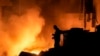 A man uses his mobile phone as flames and smoke rise at the scene of buildings hit by an Israeli airstrike in central Beirut, Lebanon, Oct. 10, 2024.