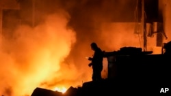 A man uses his mobile phone as flames and smoke rise at the scene of buildings hit by an Israeli airstrike in central Beirut, Lebanon, Oct. 10, 2024.