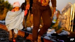 A father and his daughter cross the borderline on their way to a temporary holding center for migrants in the early morning at the border between Serbia and Hungary in Roszke, southern Hungary, Sept. 14, 2015.