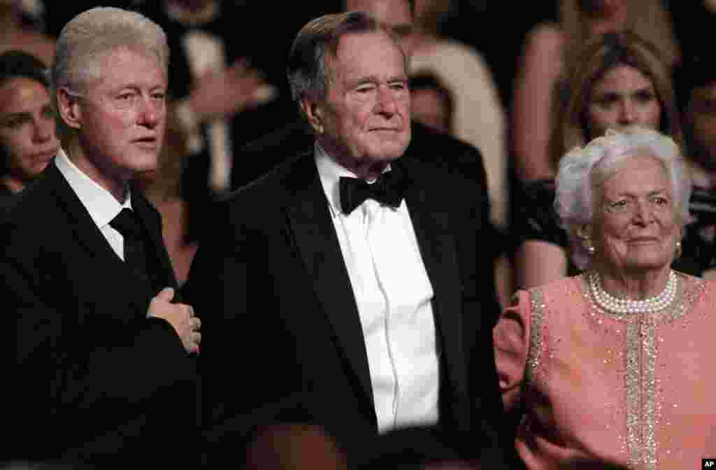 Dari kiri, mantan Presiden Bill Clinton, mantan Presiden George H.W. Bush dan istrinya Barbara Bush berdiri untuk menghormati Lagu Kebangsaan di Kennedy Center, 21 Maret 2011.