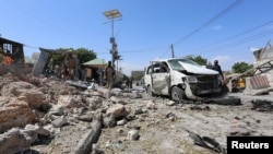 FILE - Somali policemen look at the wreckage of a destroyed car at the scene of a suicide attack at a checkpoint outside the main base of an African Union peacekeeping force in the Somali capital, Mogadishu, Jan. 2, 2017.