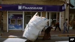 A scrap collector pulls her trolley in front of a Turkish bank in Istanbul, Tuesday, June 4, 2013. Turkey's stock market recovered slightly after plummeting amid nationwide unrest. On Monday the Borsa Istanbul 100 Index closed down 10.5 percent
