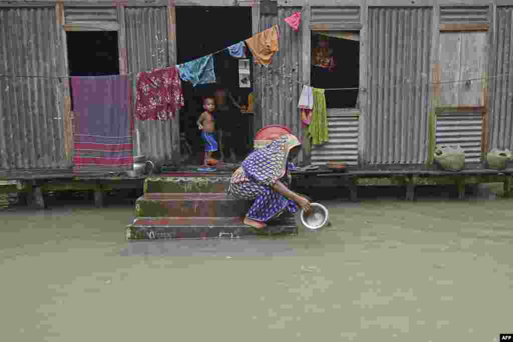 A woman washes her cooking pot in the flood waters outside her house in Sreenagar, Bangladesh.