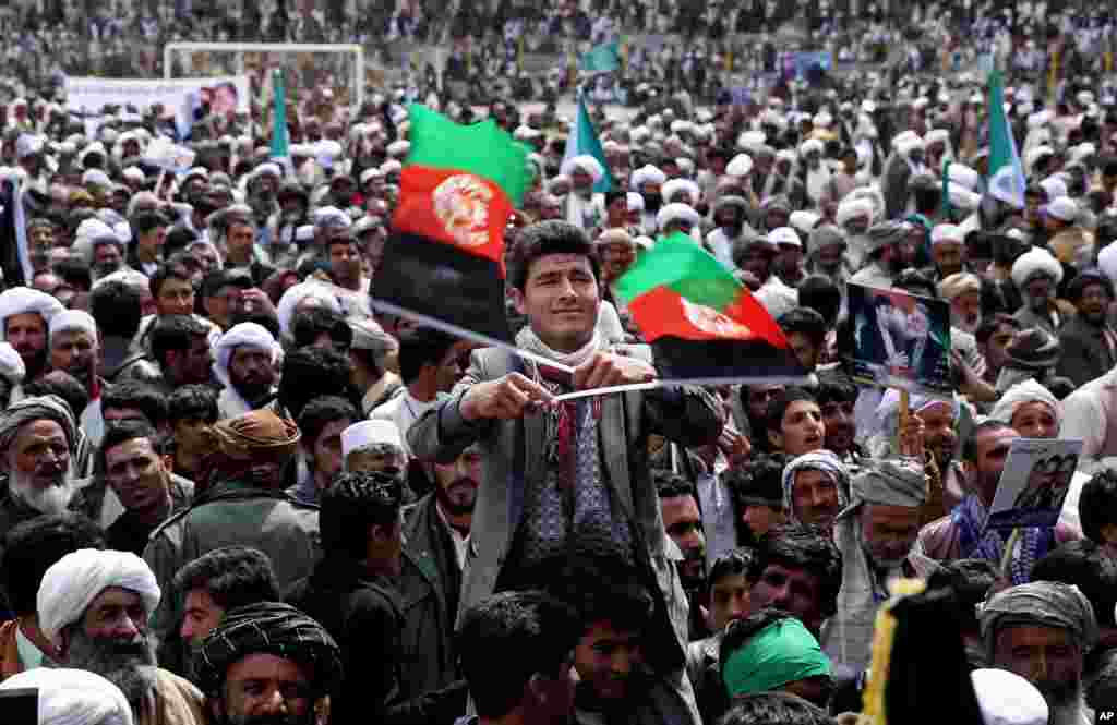 A supporter of presidential candidate and former foreign minister Zalmai Rassoul, center, waves two Afghan national flags during a campaign rally in Herat, March 30, 2014.