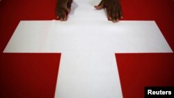 FILE - A worker displays a Swiss flag at the Fabrica de Bandeiras flag factory in Rio de Janeiro, May 29, 2014. 