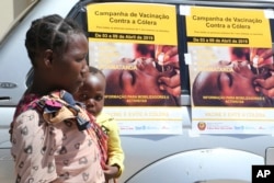 A woman and her baby walk past cholera vaccination campaign posters on the first day of the cholera vaccination program at a camp for displaced survivors of cyclone Idai in Beira, Mozambique, April, 3, 2019.