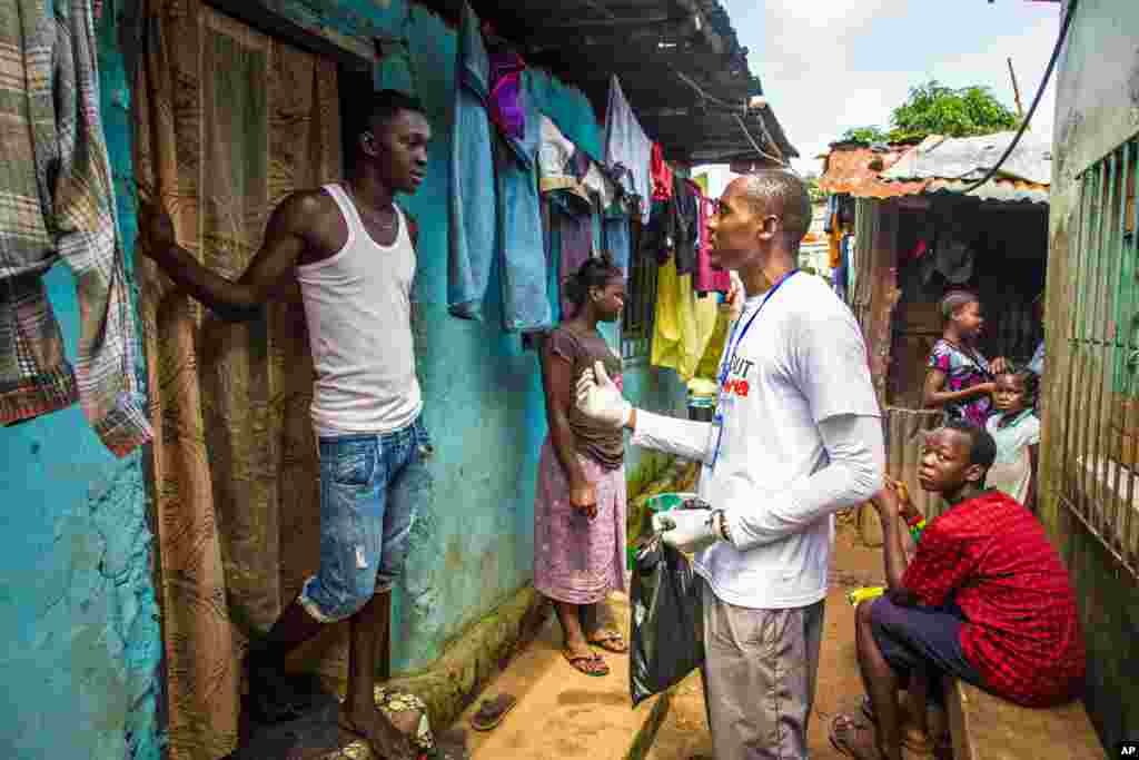 Um voluntário de saúde fala com o residente de um bairro sobre prevenção e como identificar noutros o vírus do Ébola e distribui barras de sabão em Freetown, Serra Leoa, Set. 20, 2014. 