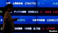 FILE - A woman walks past a screen showing market indices in Tokyo. The International Monetary Fund says that for advanced economies, debt has risen to more than 107 percent of their national economic output, while Japan is almost at 250 percent.