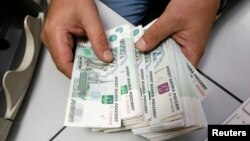 Seorang pegawai perusahaan swasta menghitung lembar uang kertas rubel di Krasnoyarsk, Siberia, 17 Desember 2014. 