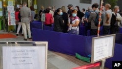 In this March 24, 2021, photo, a notice of vaccine suspension, left, is placed as people queue up outside a vaccination center for BioNTech in Hong Kong.