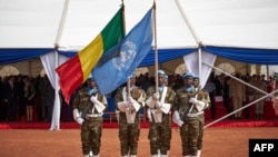 FILE - Soldiers hold the United Nations and Malian flags during the ceremony of Peacekeepers Day at the operating base of MINUSMA (The United Nations Multidimensional Integrated Stabilization Mission in Mali) in Bamako on May 29, 2018.