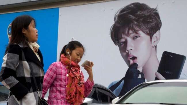 FILE - Women walk past an ad featuring teen idol Lu Han in Beijing, Oct. 21, 2017. China's government banned effeminate men on TV and told broadcasters Sept. 2, 2021, to promote