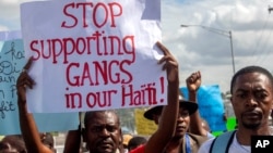 FILE - A protester holds up a sign during a rally against an increase in gang violence demonstrators say the government has proven incapable of controlling, in Port-au-Prince, Haiti, Dec. 10, 2020. 