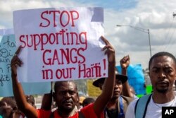 FILE - A protester holds up a sign during a rally against an increase in gang violence demonstrators say the government has proven incapable of controlling, in Port-au-Prince, Haiti, Dec. 10, 2020.