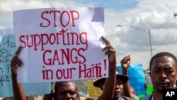 FILE - A protester holds up a sign during a rally against an increase in gang violence demonstrators say the government has proven incapable of controlling, in Port-au-Prince, Haiti, Dec. 10, 2020. 