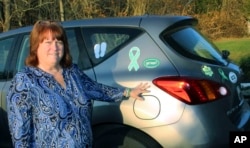 FILE - In this Nov. 30, 2017 photo, Suzanne Davenport poses beside her car on which she displays numerous stickers and magnets in memory of the 26 people killed in the December 2012 shooting at the Sandy Hook Elementary School in Newtown, Conn.