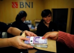 Seorang perempuan memegang uang kertas rupiah di salah satu bank keliling Bank Negara Indonesia (BNI) di Jakarta, 15 Juli 2013. (Foto: Reuters/Beawiharta)