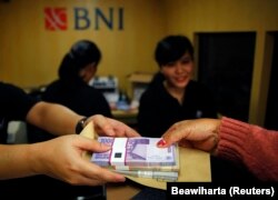 Seorang perempuan memegang uang kertas rupiah di salah satu bank keliling Bank Negara Indonesia (BNI) di Jakarta, 15 Juli 2013. (Foto: Reuters/Beawiharta)