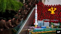 North Korean soldiers ride escalator past a model of the Unha Rocket alongside so-called "Kimjongilia" flowers at an exhibition in Pyongyang, Feb. 17, 2013.