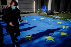 FILE - A man with a face mask and a child with an EU flag are seen at an event to garner more support for Italy during the coronavirus pandemic, in front of the Italian embassy in Berlin, Germany, April 22, 2020.