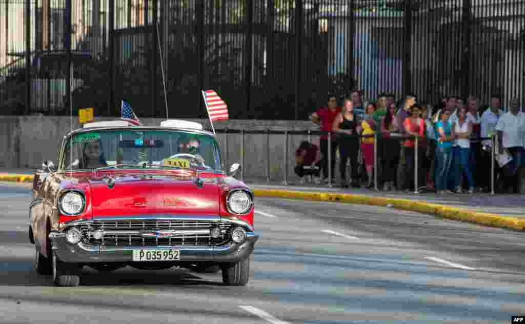 An old car with U.S. flags drives by the U.S. embassy in Havana. The United States and Cuba formally resumed diplomatic relations, as the Cuban flag was raised at the U.S. State Department in a historic gesture toward ending decades of hostility.