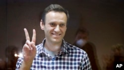 FILE - Russian opposition leader Alexey Navalny gestures as he stands in a cage in the Babuskinsky District Court in Moscow, Feb. 20, 2021.