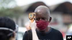 Un miembro de la Cruz Roja toma la temperatura de un trabajador del principal mercado de distribución de Río de Janeiro, Brasil. Junio 23 de 2020.