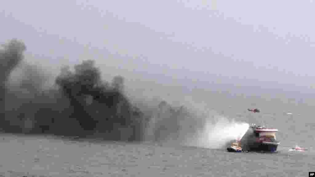 In this image provided by the Italian Navy, a helicopter hovers above the Italian-flagged Norman Atlantic, shown billowing smoke, after it caught fire in the Adriatic Sea, Dec. 28, 2014. 